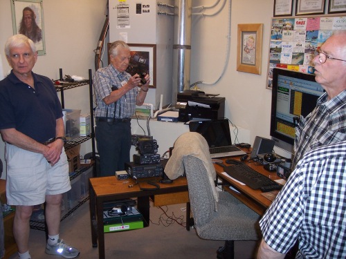 The Aspens Amateur Radio Club, K5ASP, shack is in a maintenance room on the third floor of the lodge. One of two operating positions is visible. This position includes a modern solid-state transceiver, a software defined radio (SDR), and a computer with an extra large display. A printer next to the air-conditioning unit provides convenient printouts from the computer. QSL cards received from contacted amateur radio stations are displayed on the wall. 