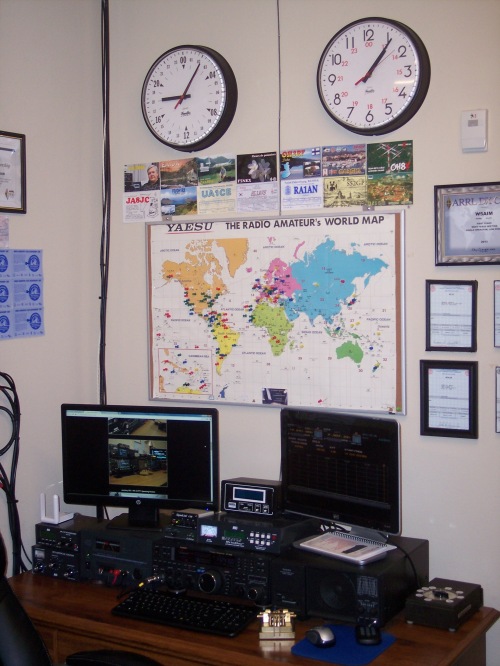 One of two operating positions in the K5ASP amateur radio shack. This includes two-way amateur radio equipment and computer. Wall clocks display Coordinated Universal Time (UTC) and local time. Flags on the wall map of the world indicate locations of stations contacted by K5ASP. 